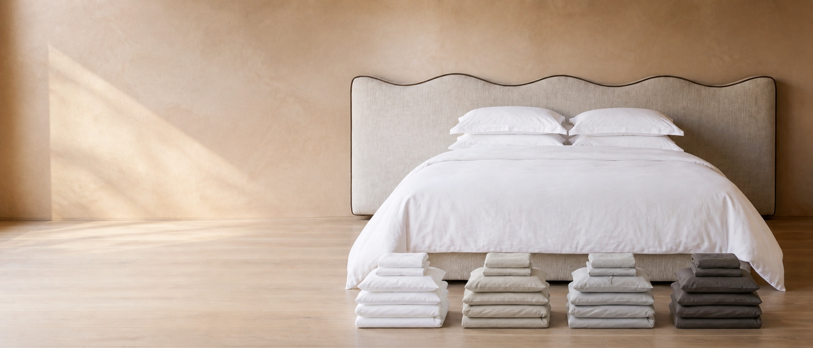 Muze bedding bundles in White, Stone, Light Grey and Charcoal at the foot of an upholstered bed